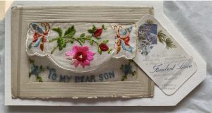 An embroidered silk postcard decorated with embroidered flowers, with text that reads 'to my dear son'.
