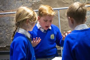 Three school children discussing a mystery object in front of a mosaic