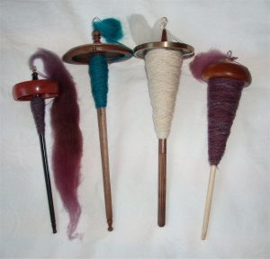 Photo of 4 drop Spindles, each with wooden stick, weight at one end and yarn wrapped around the stick