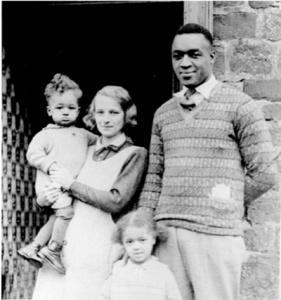 Image of boxer Larry Gains with his wife and two children, standing in the doorway of a house