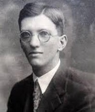 Photograph of a young man wearing a suit and tie and round glasses