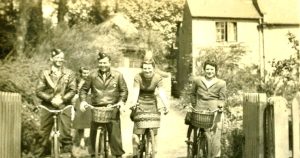 Two men and two women on bicycles in front of a cottage